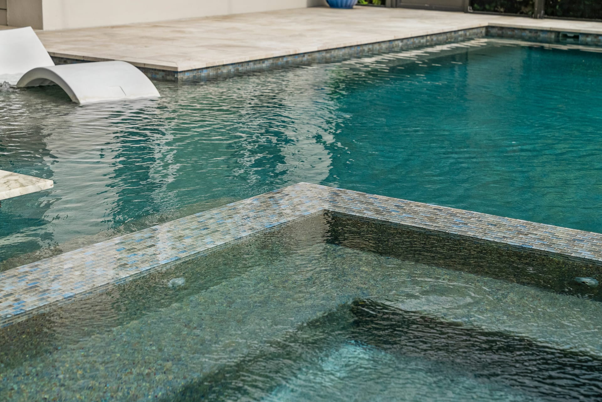Spillover spa with water cascading into pool below, warm LED lighting at dusk