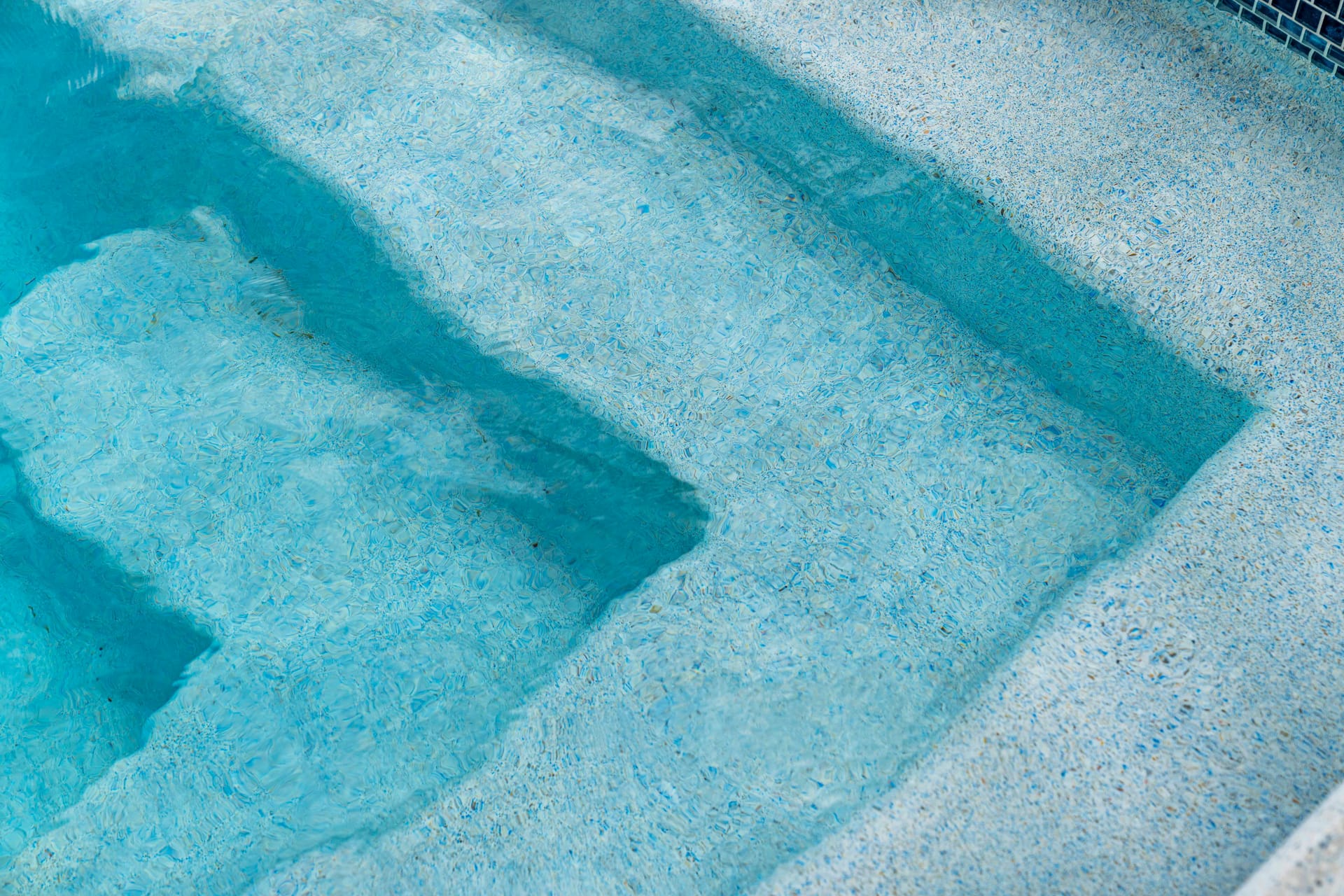 Pebble finish pool interior in sunlight, aggregate texture with warm lagoon-like water color